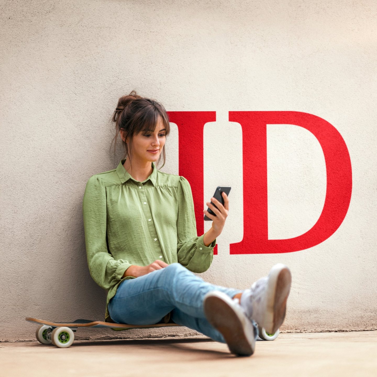 Young woman sitting on skateboard, using smartphone