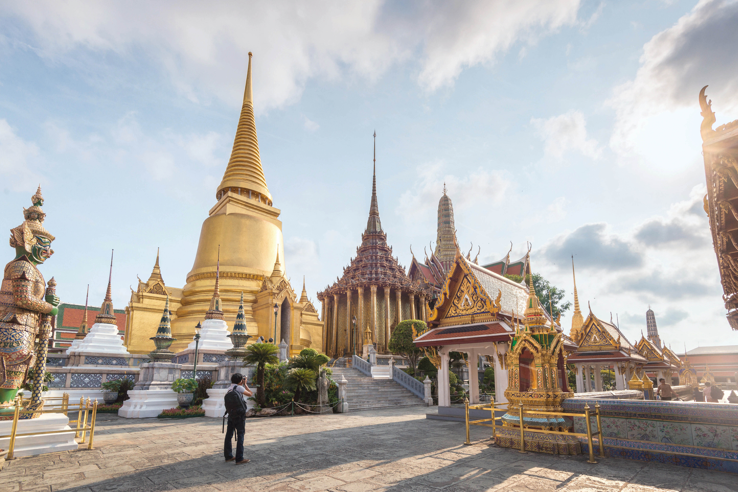 Traveller shooting Wat Phra Kaew. A shot of of Grand Stupa and Phra ubosot of Wat Phra Kaew with Tosakan (a green Ramayana Giant on the left of the picture). Wat Phra Kaew or Temple of the Emerald Buddha is highly regarded as the most sacred Buddhist temple in Thailand. This temple a top tourist attraction in Bangkok, Thailand, Southeast Asia.