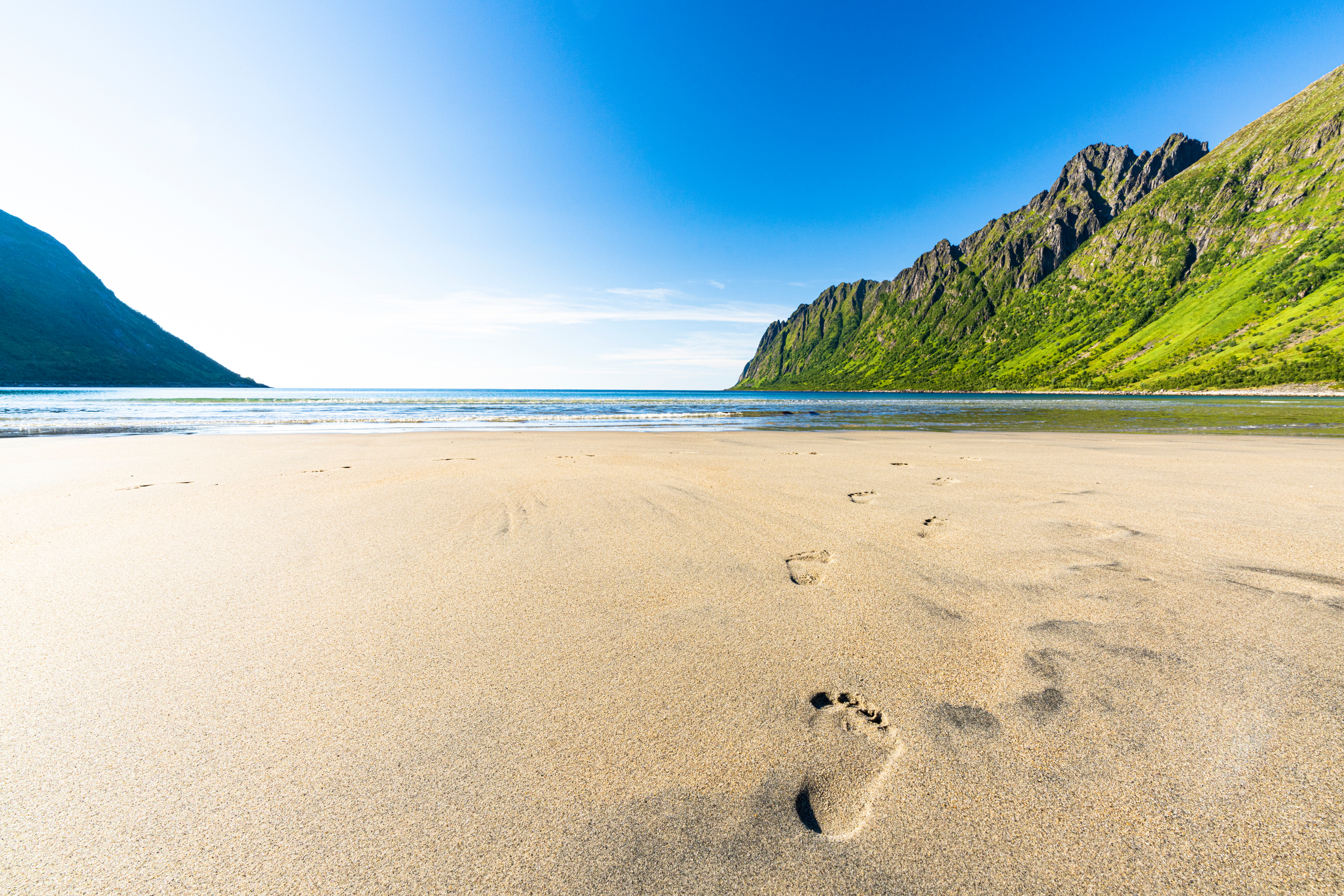 Sun shining over Ersfjord beach and fjord during summer with footprints in the sand, Senja, Troms county, Norway