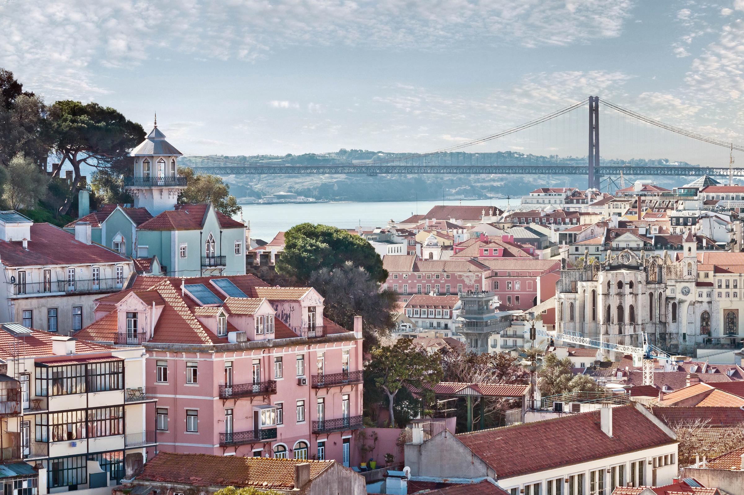 The lisbon skyline with the Ponte 25 de Abril suspension bridge which spans the river Tagus in the background. To the left is the old part of the city (the Alfama district) and to the right you can see the Elevador de santa Justa and the ruins of the Carmo Convent.