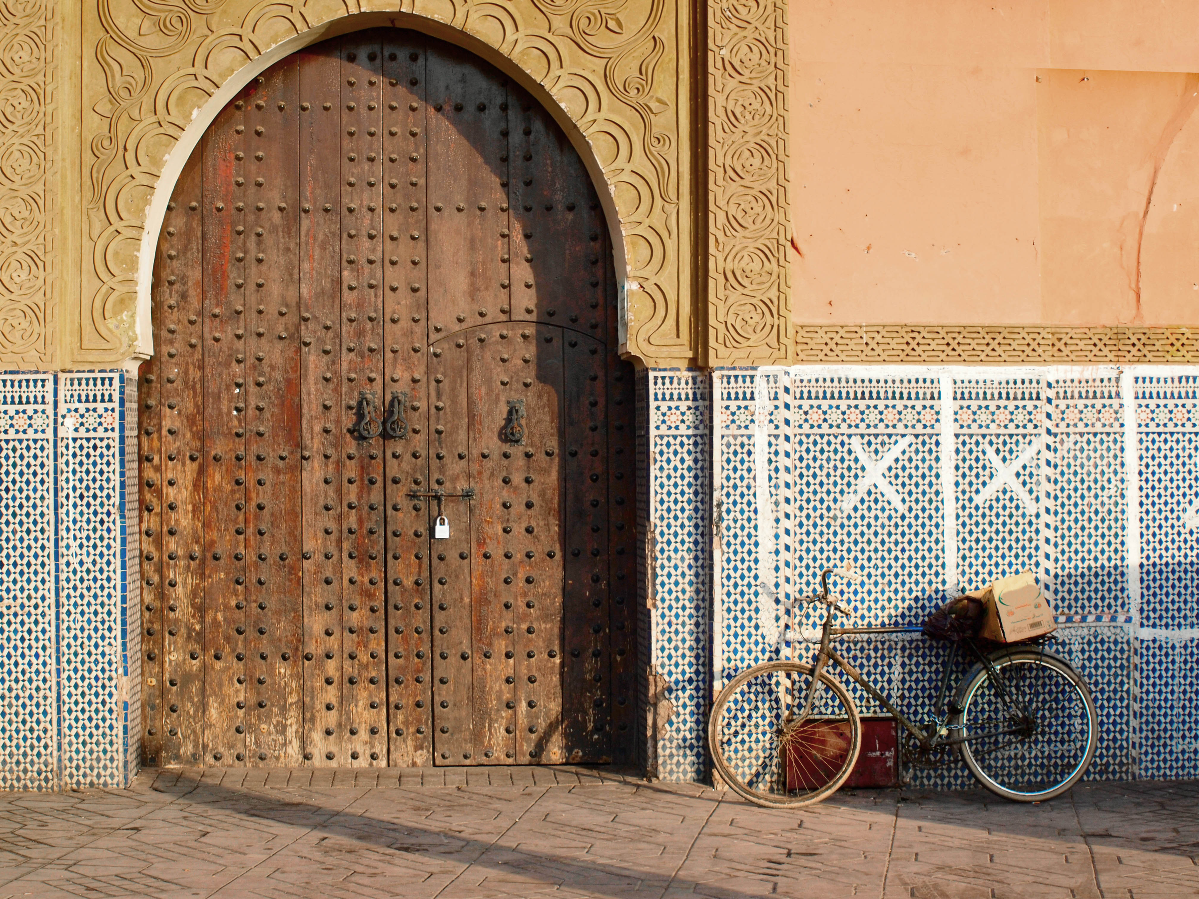 A bycicle parked outside of a building and beside of the wood front door entrance.