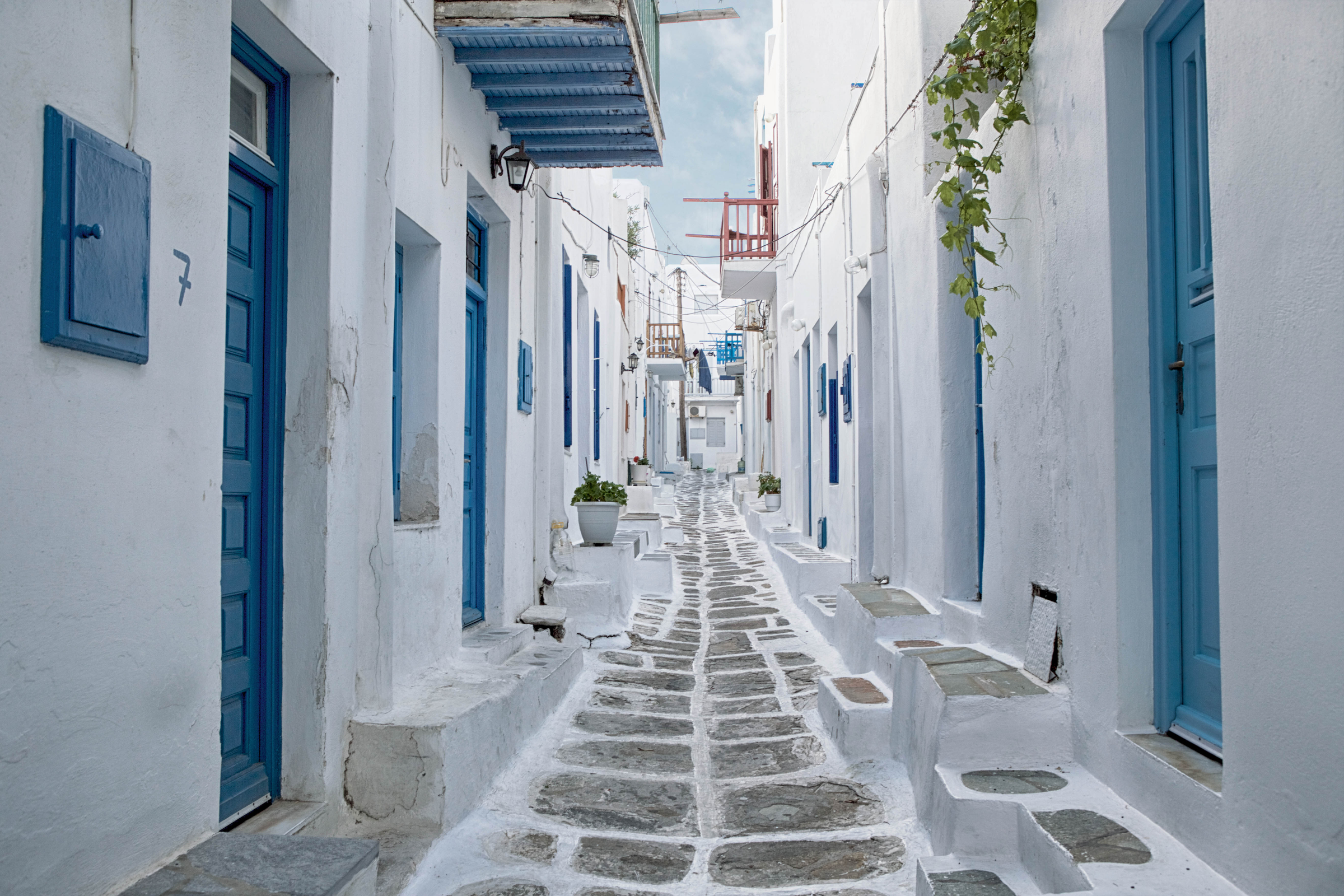 An alley in Mykonos lined with white-washed buildings with blue doors and windows, typical features of architecture found in the Cyclades Islands.