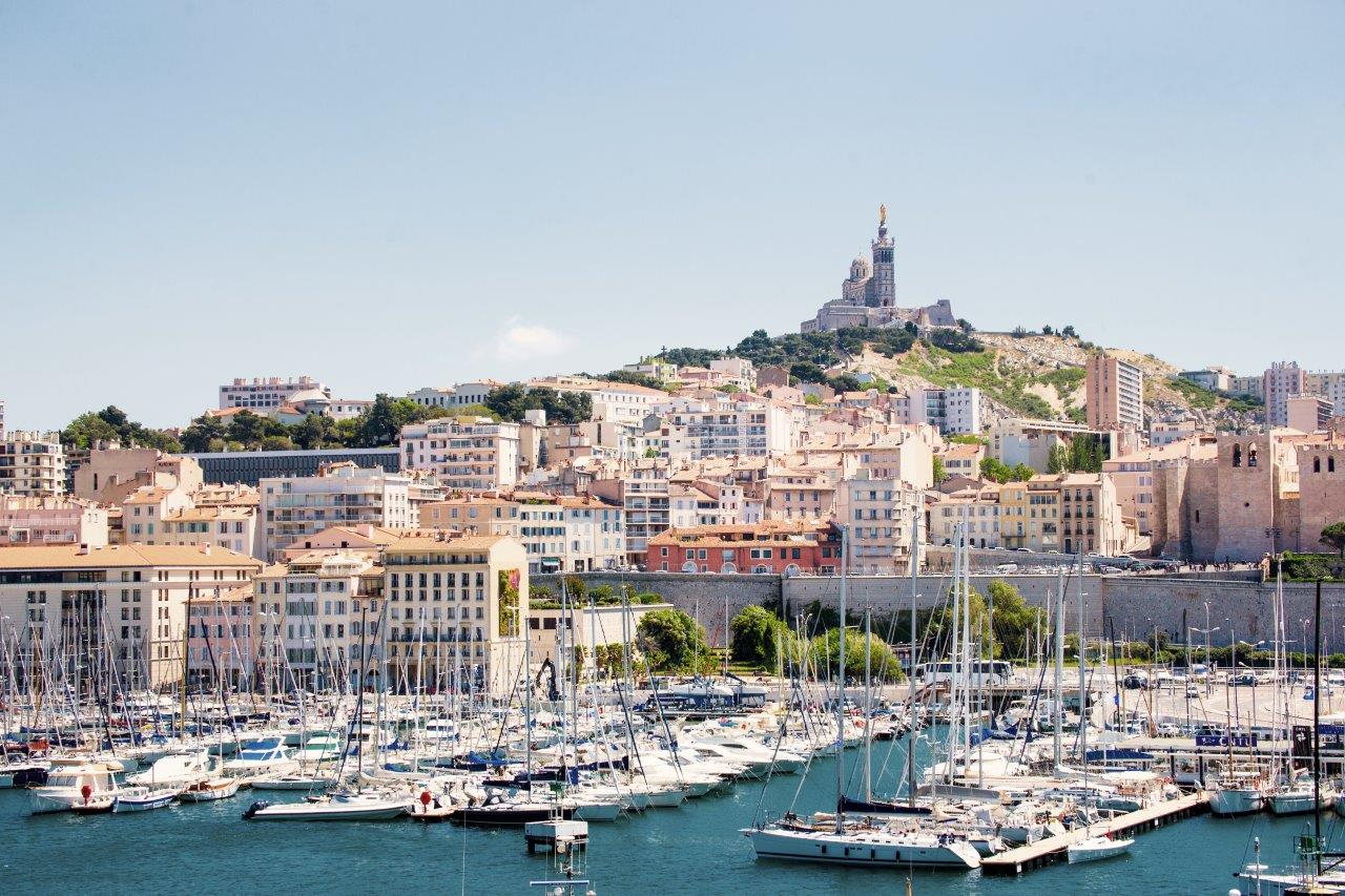 High angle view of cityscape by sea. Notre Dame de la Garde in Marseille against clear sky. Buildings by seascape on sunny day.