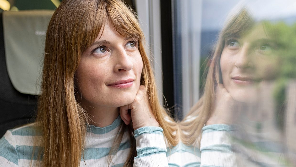 Frau sitzt in der Bahn und schaut aus dem Fenster