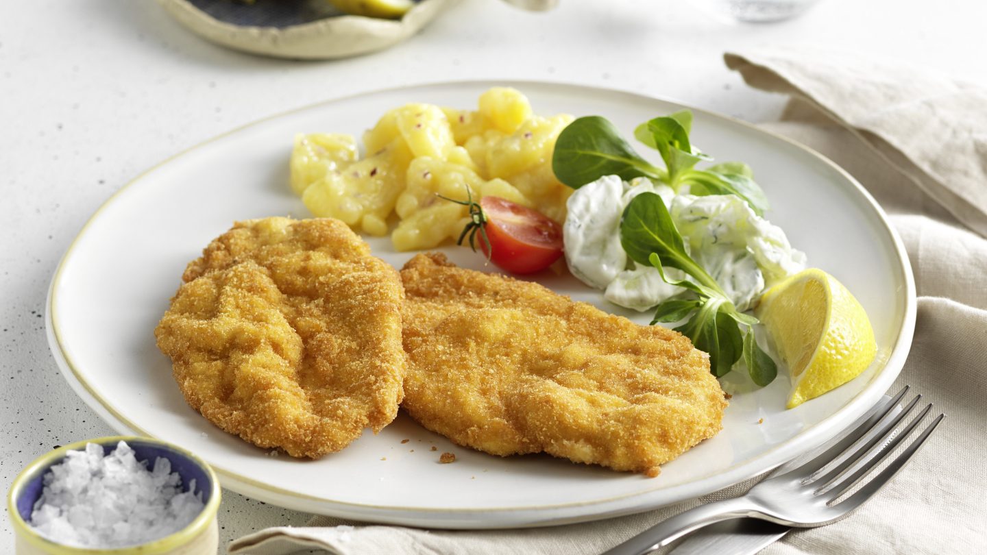 A schnitzel with potatoes and cucumber salad.