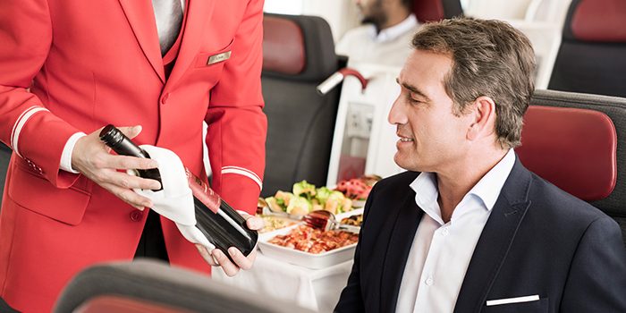 A flight attendant presents a bottle of wine to the passenger