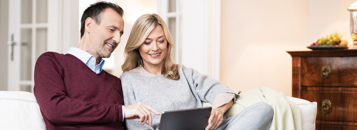 A couple is sitting on the sofa with a tablet